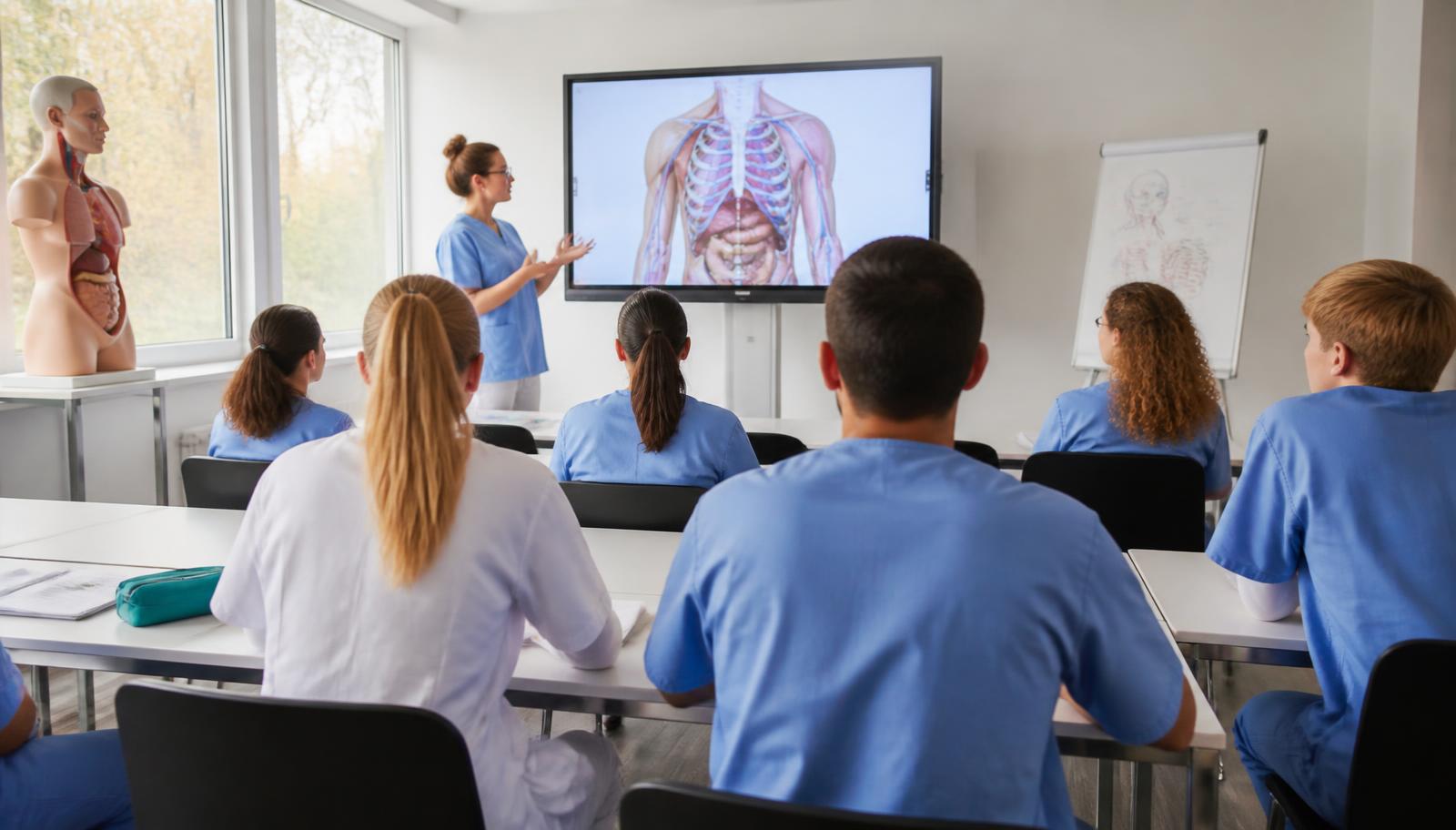 Pflegeschülerinnen und Pflegeschüler in einem modernen Schulungsraum, eine Dozentin erklärt an einem Bildschirm